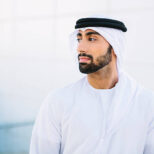 Close up portrait of Emirati businessman looking away from the camera. Wearing traditional clothing - kandura, kaffiyeh and agal. Business building in the background.